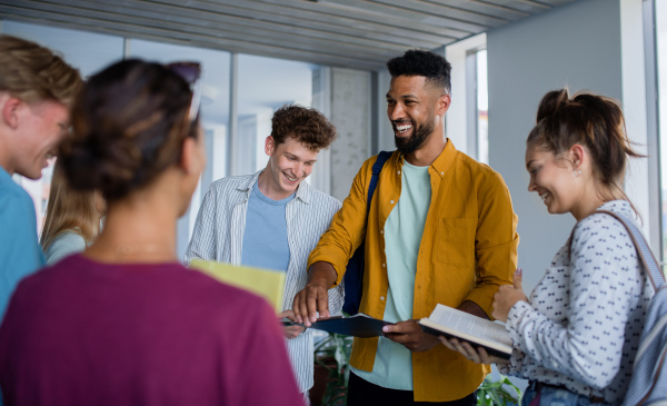 Group of cheerful university students standing in corridor indoors, talking and laughing.