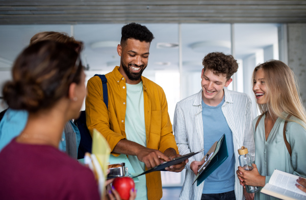 Group of cheerful university students standing in corridor indoors, talking.