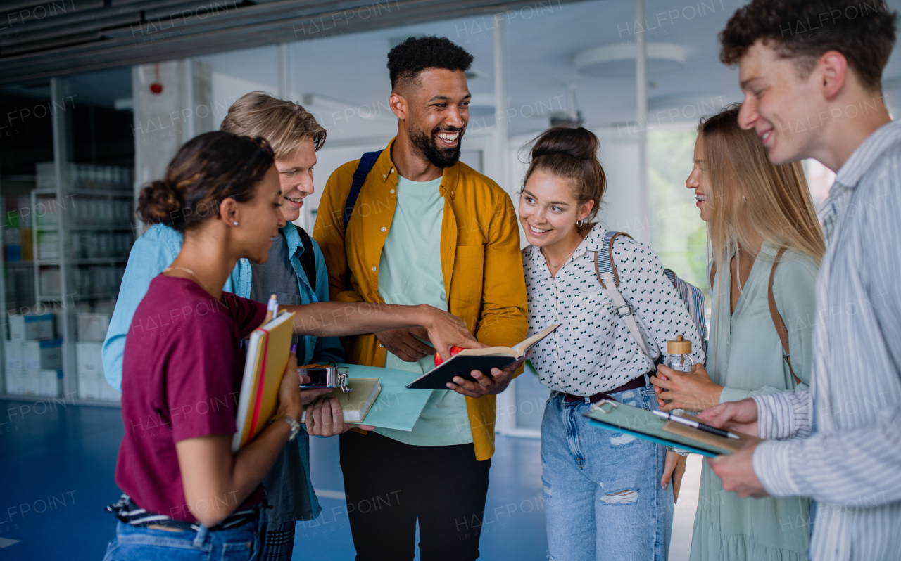 Group of cheerful university students standing in corridor indoors, talking and laughing.