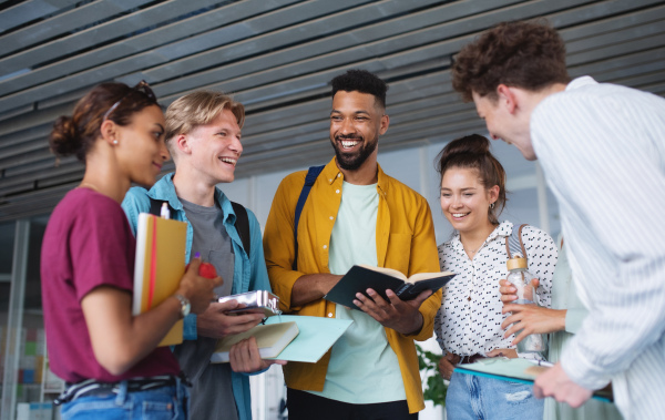 Group of cheerful university students standing in corridor indoors, talking and laughing.