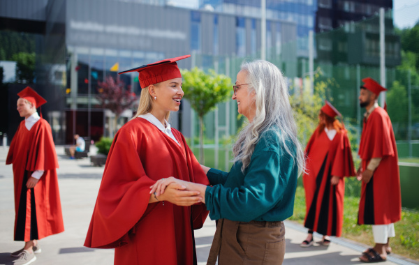 A portrait of cheerful university student with mother celebrating outdoors, graduation concept.