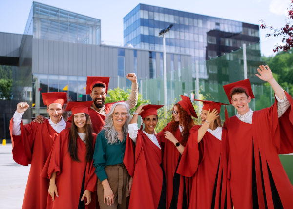 A group of cheerful university students with teacher celebrating outdoors, looking at camera, graduation concept.