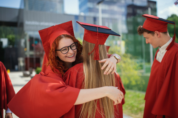 Cheerful university students friends celebrating and hugging outdoors, a graduation concept.