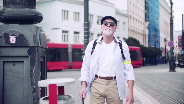 Senior blind man with white cane walking on pavement in city. Slow motion.