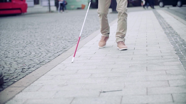 Midsection of unrecognizable blind man with white cane walking on pavement in city. Slow motion.