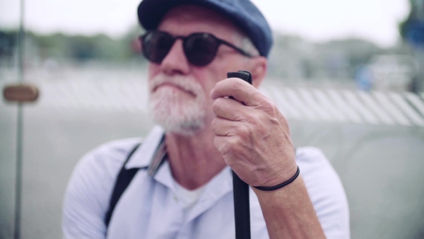 A senior blind man with white cane waiting at bus stop in city. Slow motion.