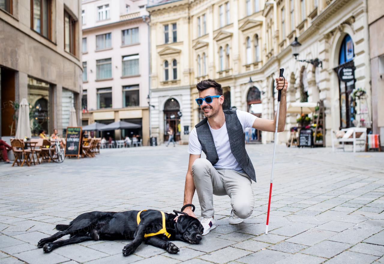 A young blind man with white cane and guide dog on pedestrian zone in city.