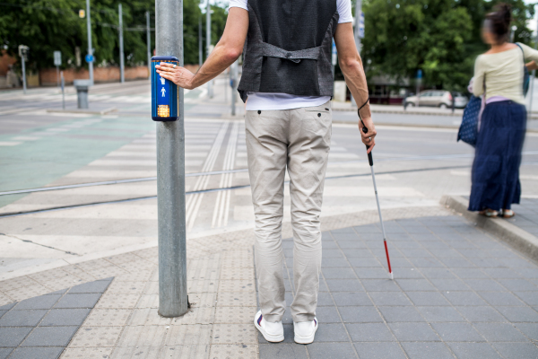 Midsection of blind man with white cane at pedestrain crossing beeping signal in city.