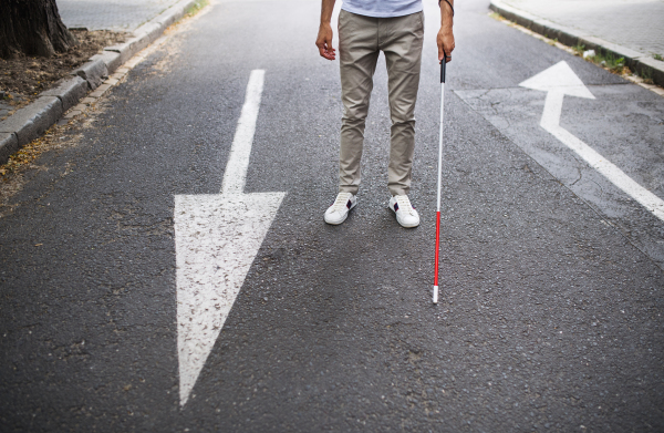 Midsection of young unrecognizable blind man with white cane walking on the street in city.