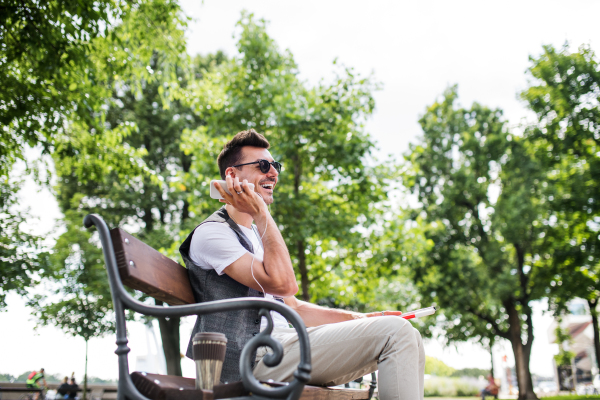 A young blind man with smartphone sitting on bench in park in city, making phone call.