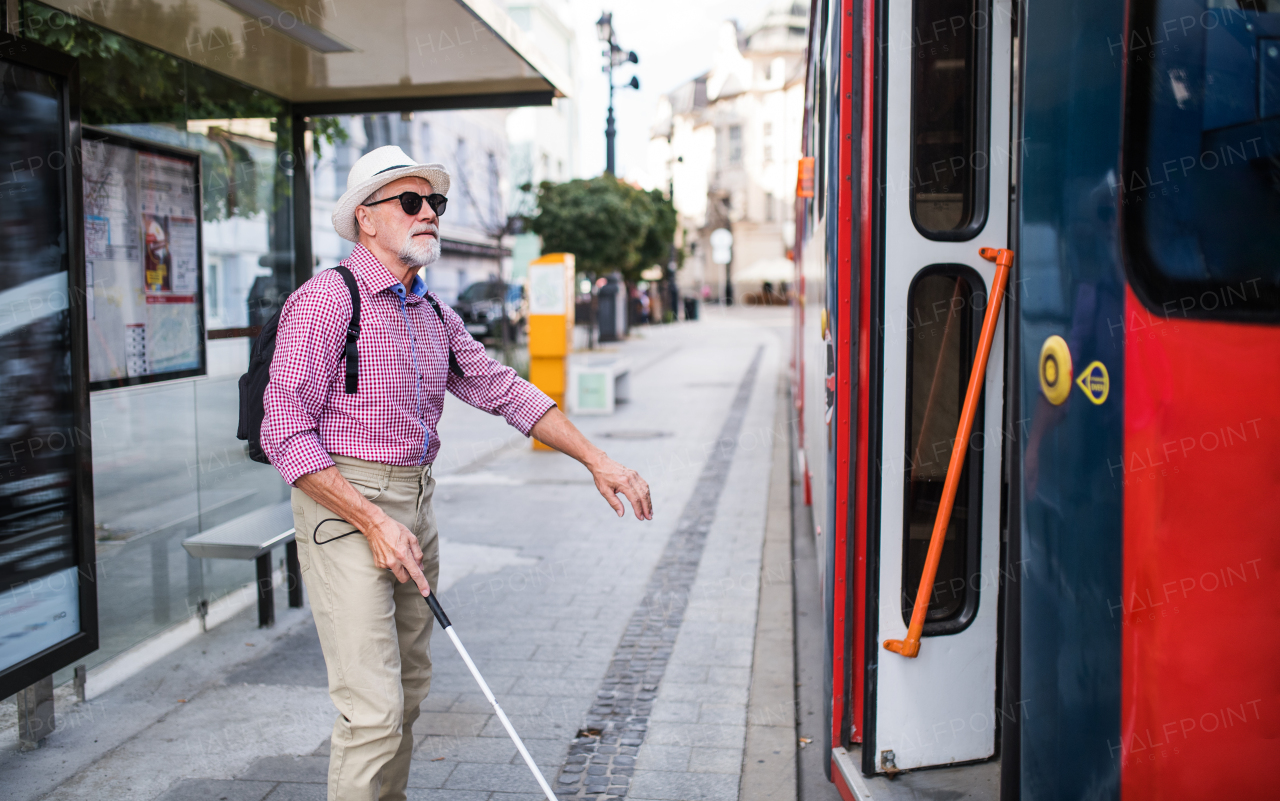 A senior blind man with white cane getting on public transport in city.