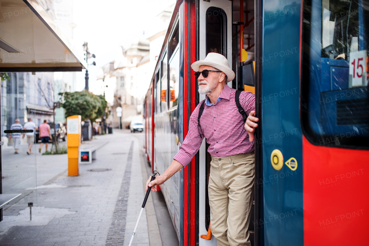 A senior blind man with white cane getting out of public transport in city.