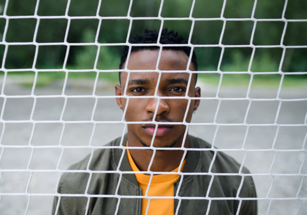 Frustrated young black man behind net outdoors in city, black lives matter and discrimination concept.