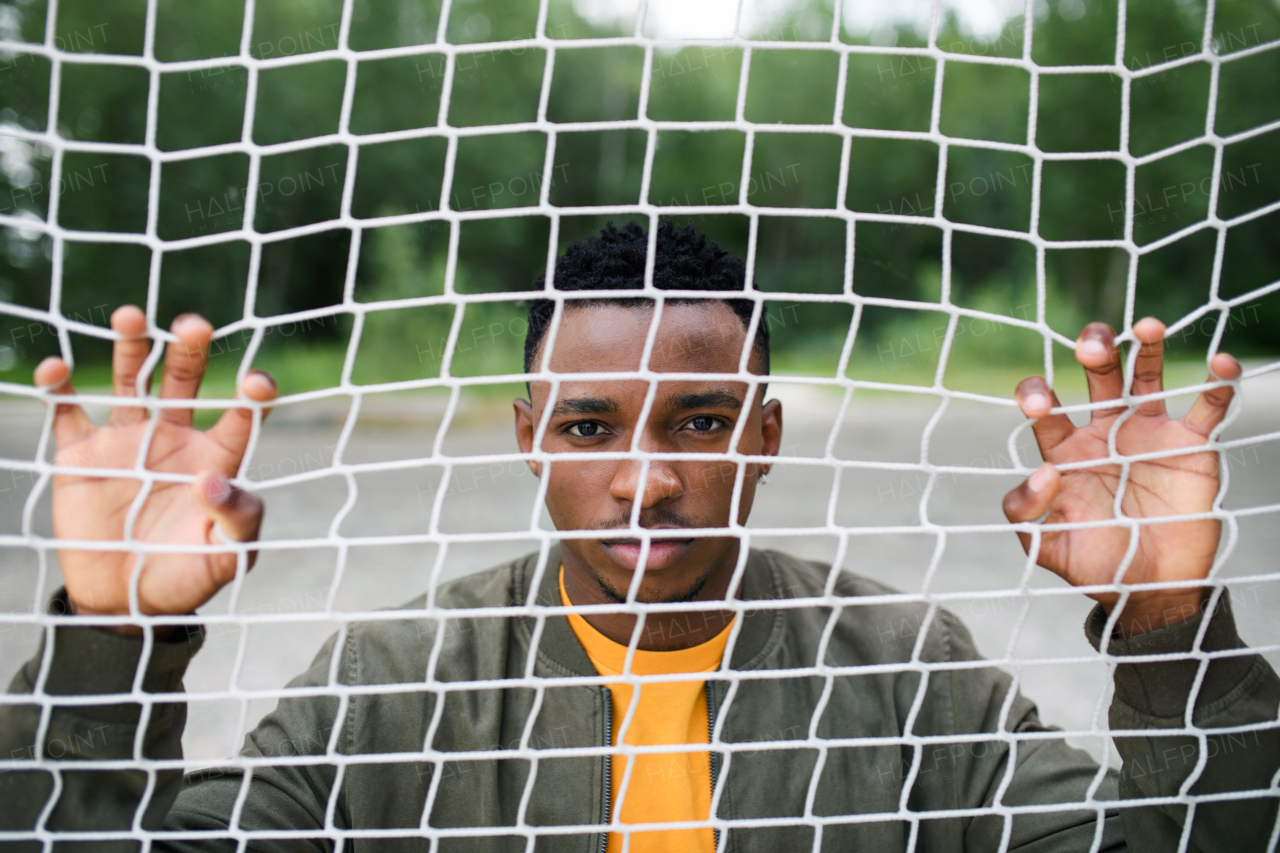 Frustrated young black man behind net outdoors in city, black lives matter and discrimination concept.