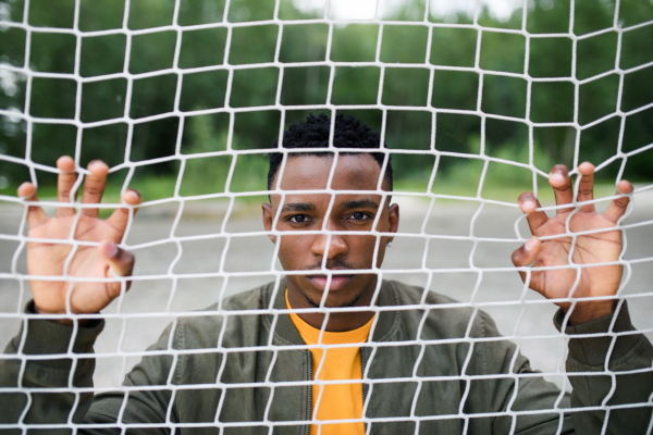 Frustrated young black man behind net outdoors in city, black lives matter and discrimination concept.