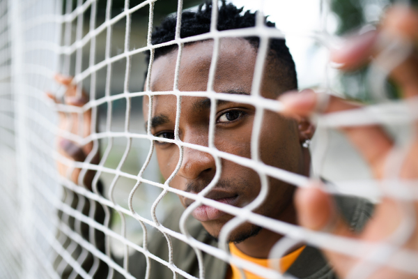 Frustrated young black man behind net outdoors in city, black lives matter and discrimination concept.