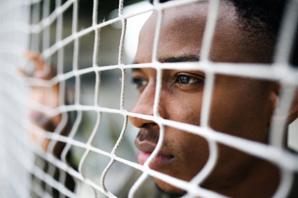 Frustrated young black man behind net outdoors in city, black lives matter and discrimination concept.