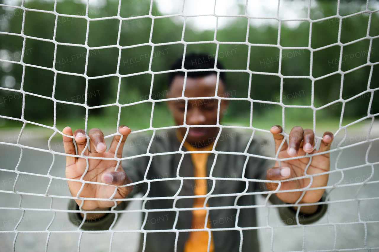 Frustrated young black man behind net outdoors in city, black lives matter and discrimination concept.