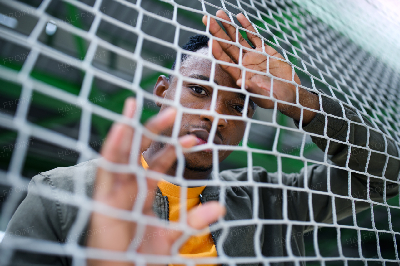 Frustrated young black man behind net outdoors in city, black lives matter and discrimination concept.