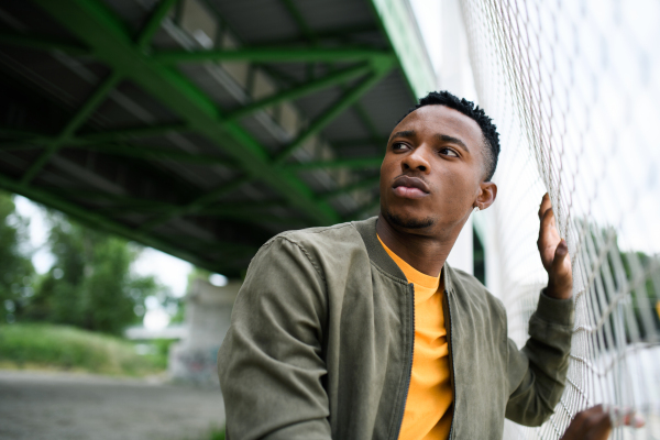 Frustrated young black man behind net outdoors in city, black lives matter and discrimination concept.