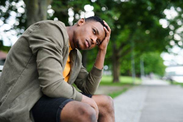 Sad and frustrated young black man sitting on bench outdoors in city, black lives matter concept.