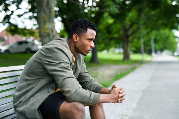 Sad and frustrated young black man sitting on bench outdoors in city, black lives matter concept.