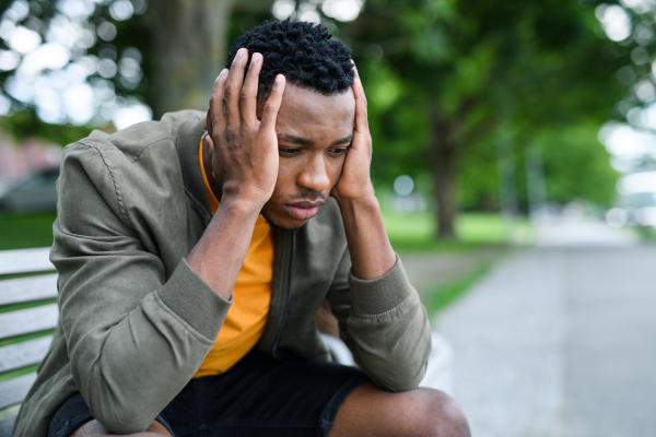 Sad and frustrated young black man sitting on bench outdoors in city, black lives matter concept.