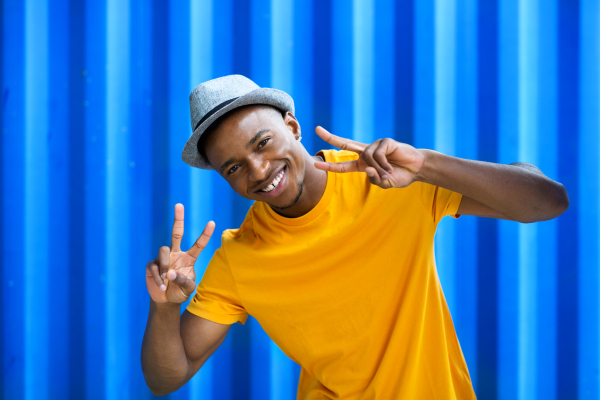 Cheerful young black man standing against blue background, peace gesture and black lives matter concept.