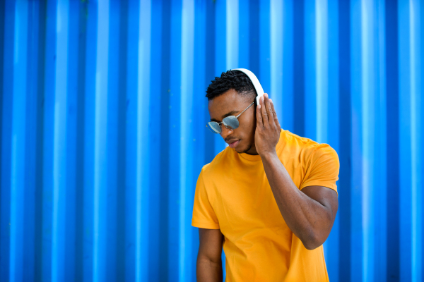 Young black man with sunglasses and headphones standing against blue background, black lives matter concept.