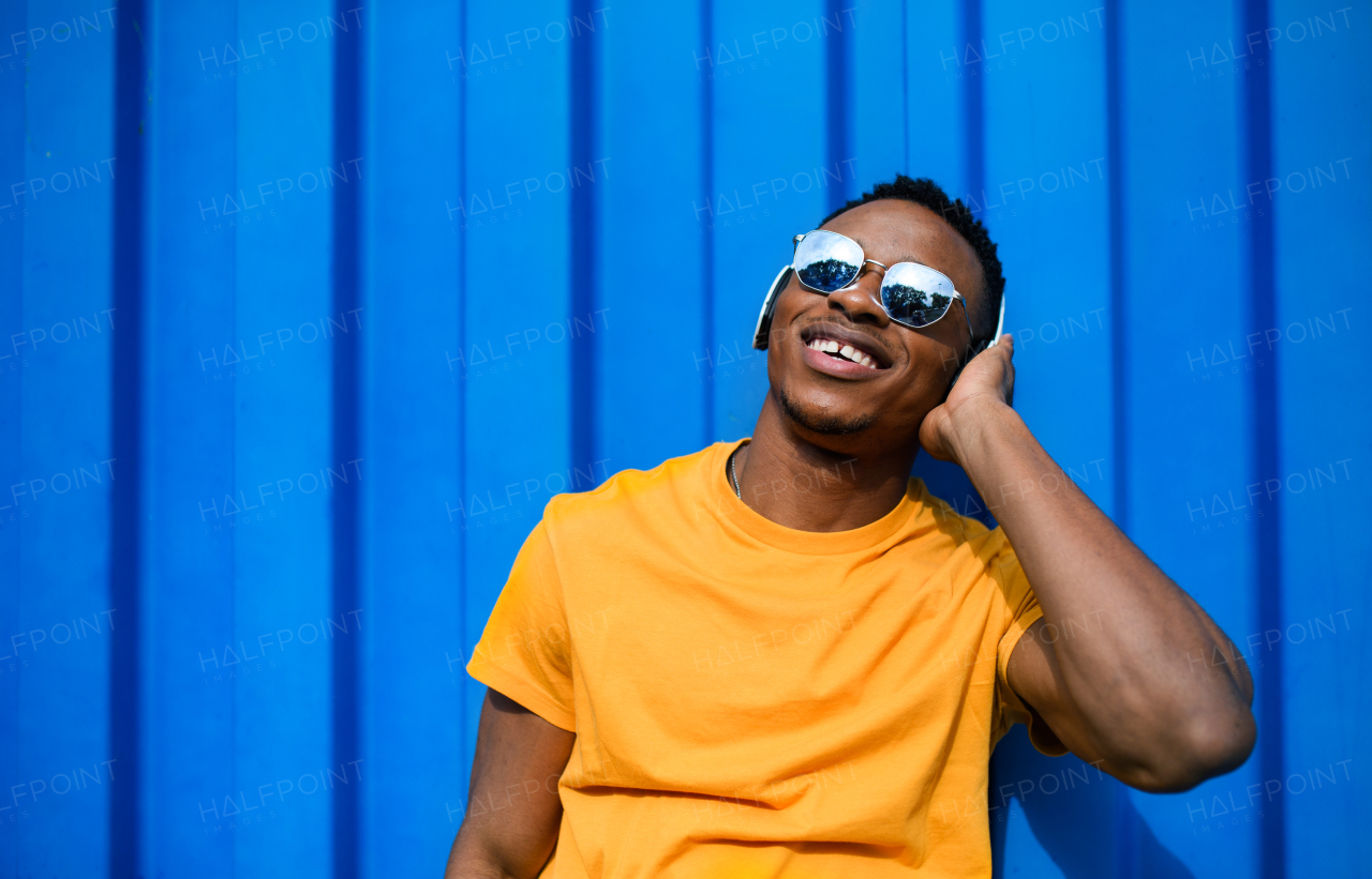 Young black man with sunglasses and headphones standing against blue background, black lives matter concept.