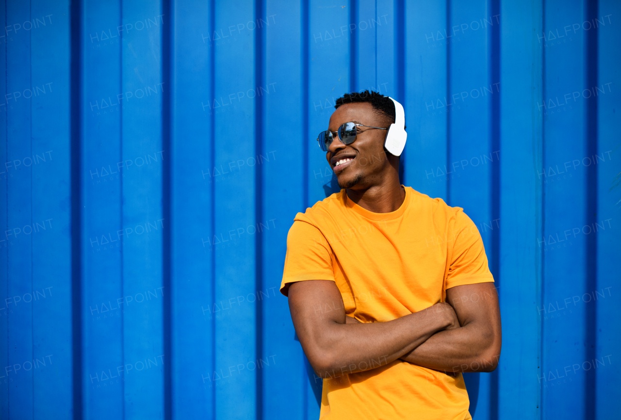 Young black man with sunglasses and headphones standing against blue background, black lives matter concept.