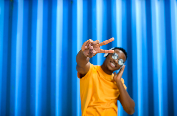 Cheerful young black man standing against blue background, peace gesture and black lives matter concept.