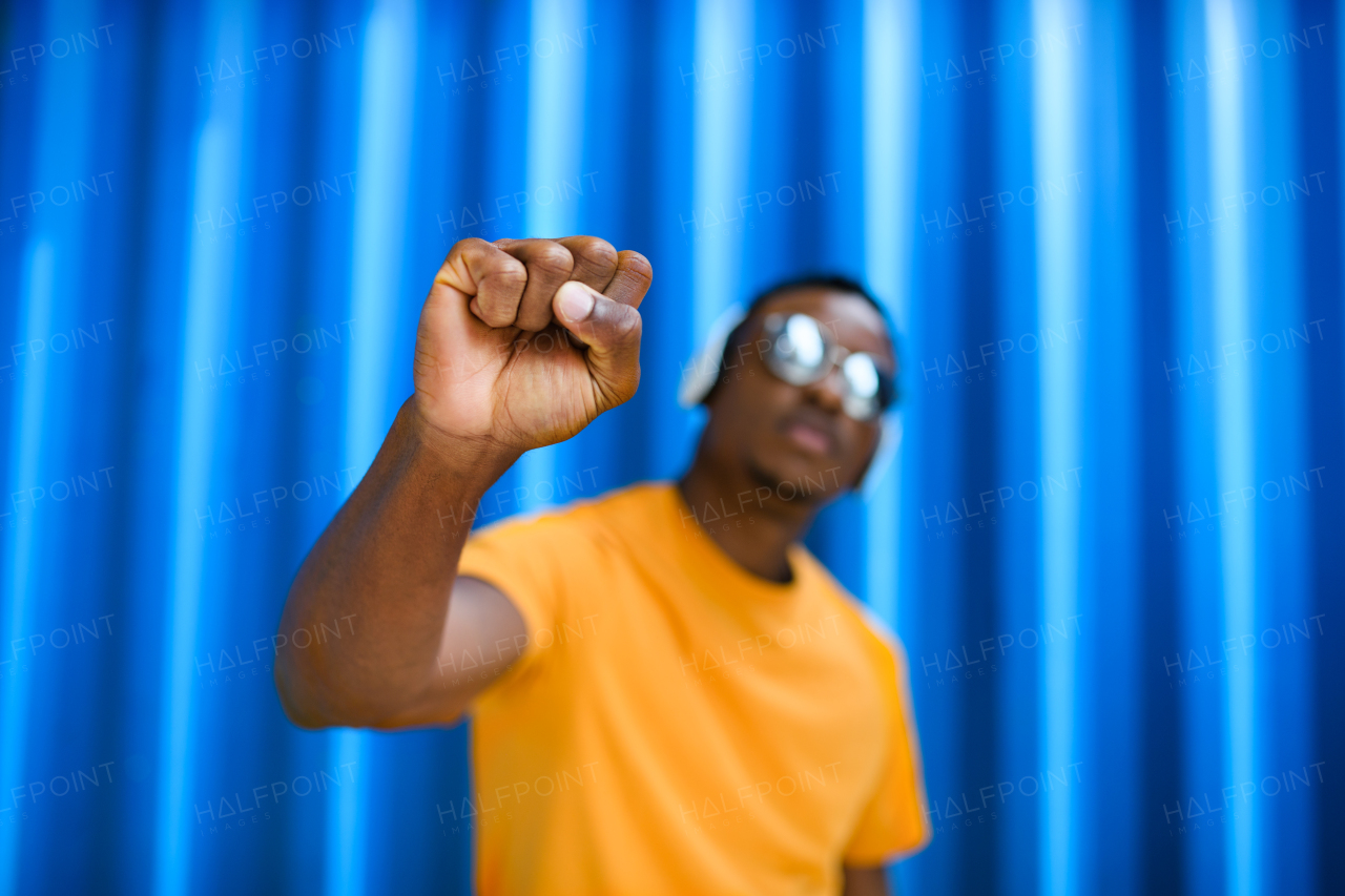 Young black man with raised fist standing against blue background, black lives matter concept.