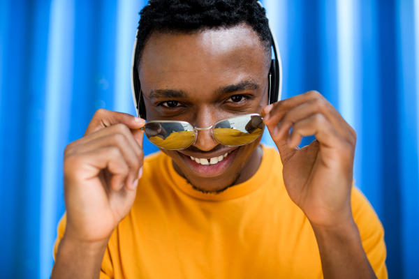 Young black man with sunglasses and headphones standing against blue background, black lives matter concept.