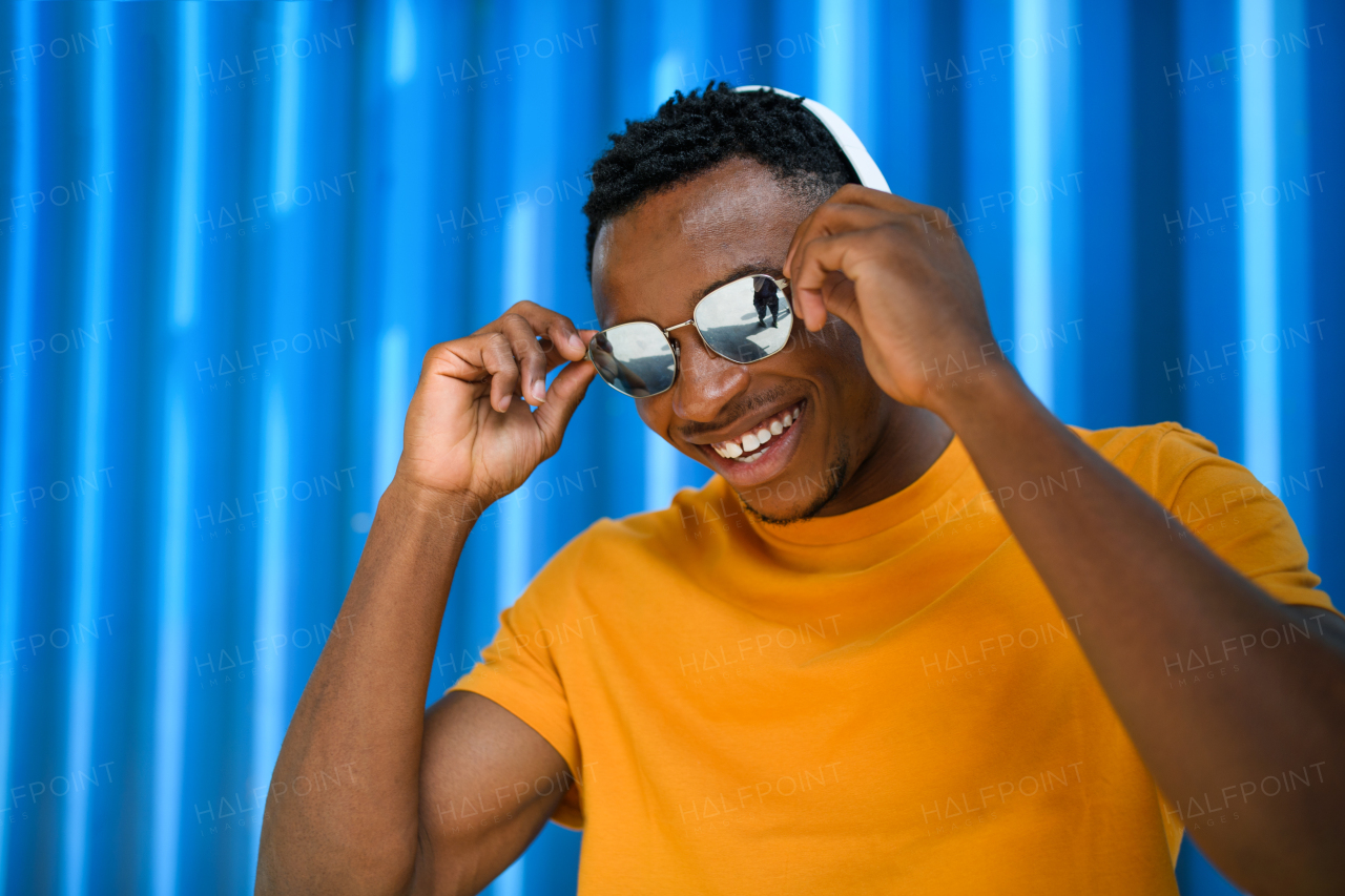 Young black man with sunglasses and headphones standing against blue background, black lives matter concept.