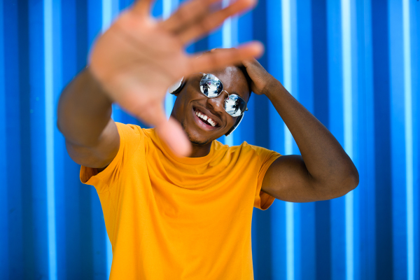 Young black man with sunglasses and headphones standing against blue background, black lives matter concept.