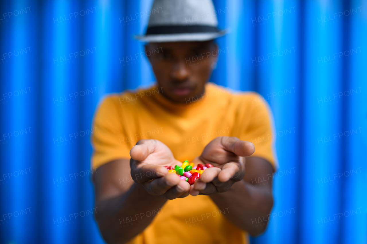 Portrait of man with skittles standing against blue background, black lives matter concept.