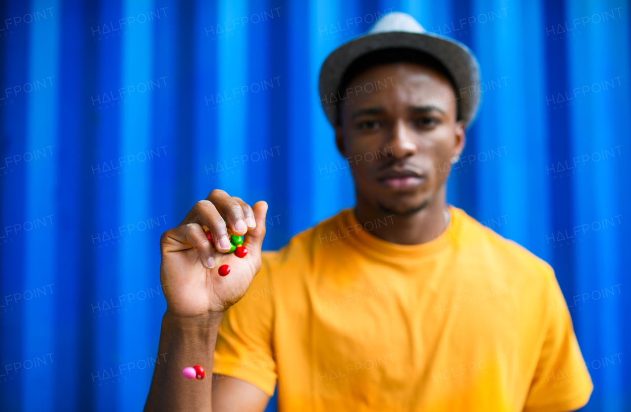 Portrait of man with skittles standing against blue background, black lives matter concept.