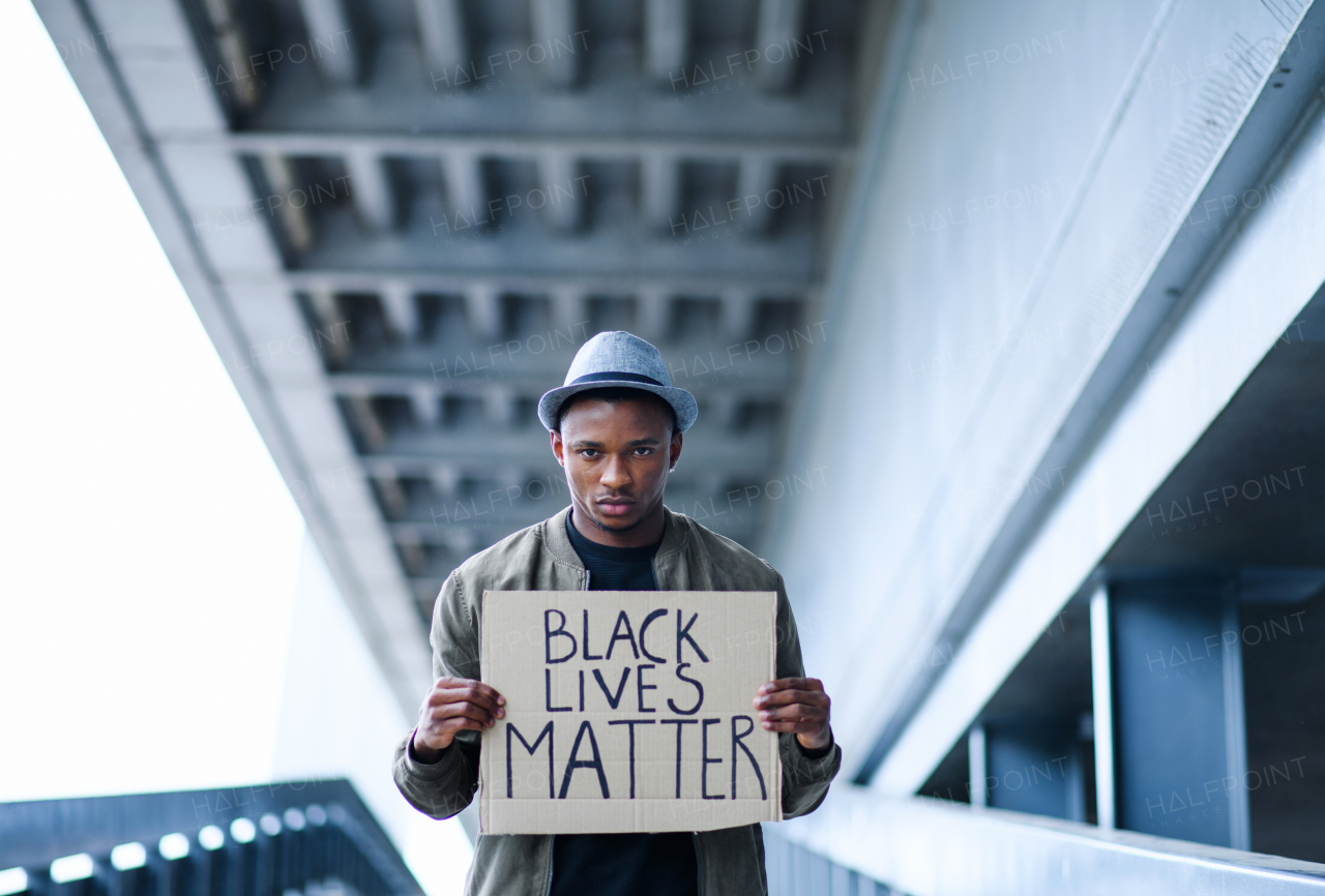 Young man with BLM sign standing outdoors in city, black lives matter concept.