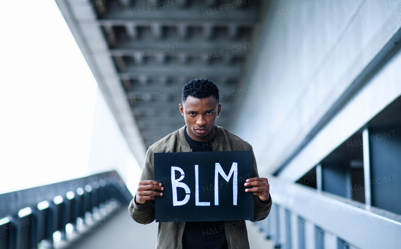 Young man with BLM sign standing outdoors in city, black lives matter concept.