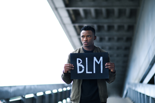 Young man with BLM sign standing outdoors in city, black lives matter concept.