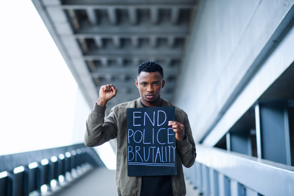 Young man with raised fist standing outdoors in city, black lives matter concept.