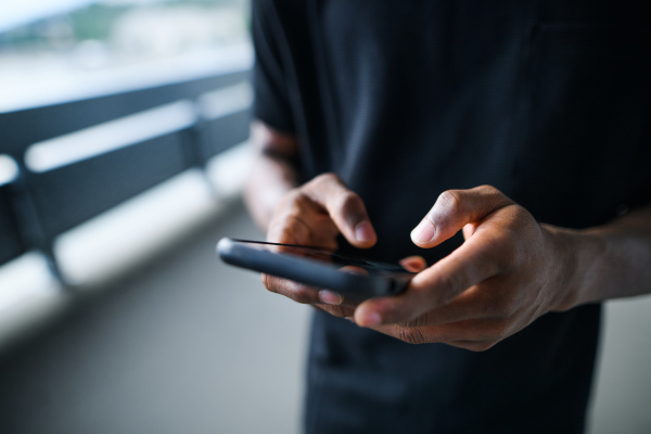 Midsection of unrecognizable black man outdoors in city, using smartphone.