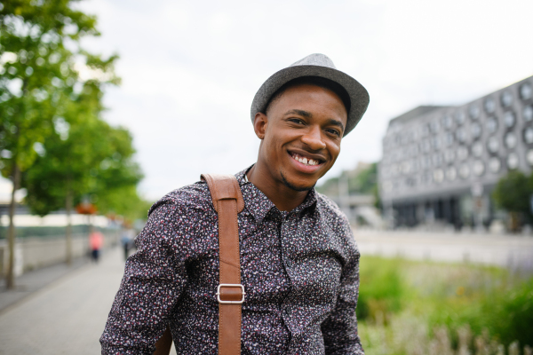 Cheerful young black man commuter outdoors in city, walking and looking at camera.