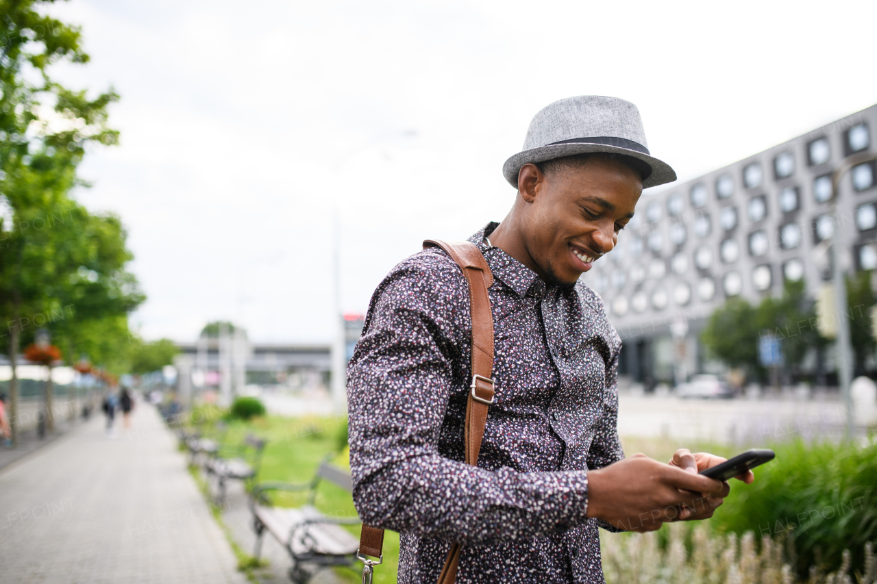 Cheerful young black man commuter with smartphone outdoors in city, walking.