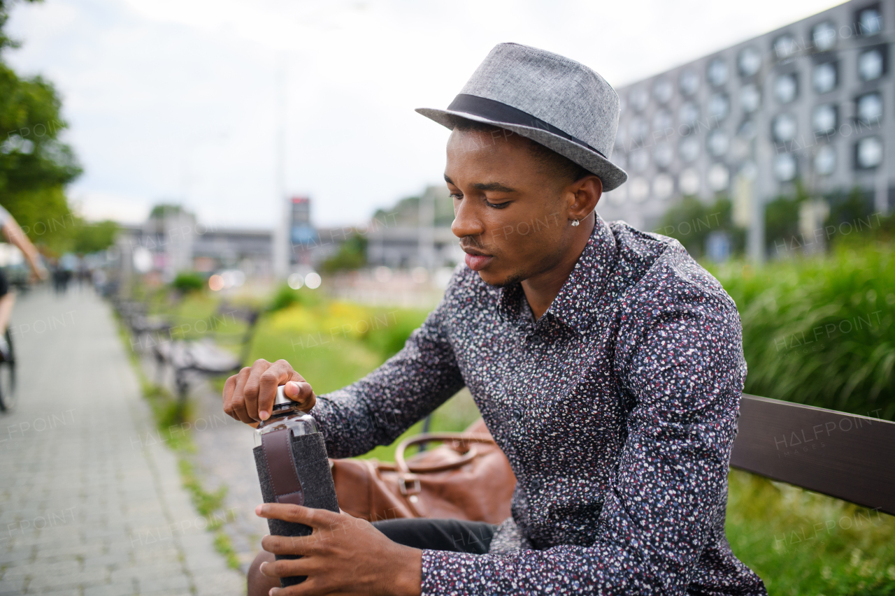 Cheerful young black man commuter sitting on bench outdoors in city, resting.