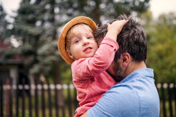 A close-up of unrecognizable father with toddler boy standing outdoors in garden in summer.