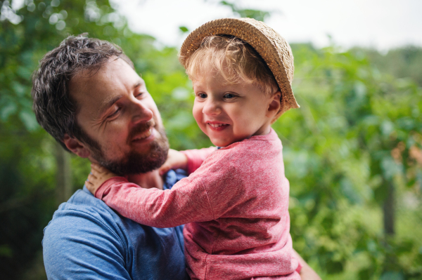 A close-up of happy father with toddler boy standing outdoors in garden in summer.