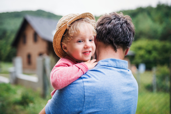 A close-up of unrecognizable father with toddler boy standing outdoors in garden in summer.