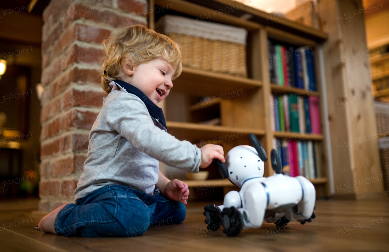 A happy cute toddler boy standing indoors at home, playing with robotic dog.